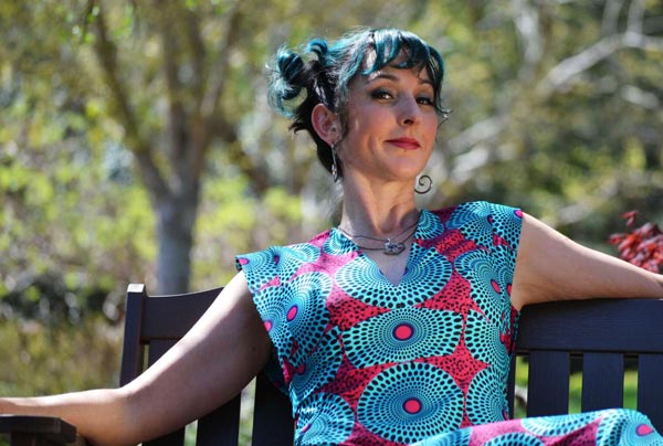 Tricia sitting on a park bench wearing a red and blue hand-made dress